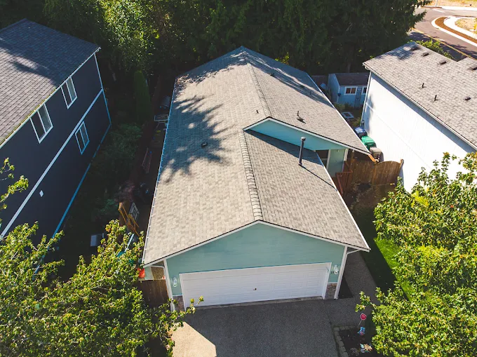 Aerial view of a rambler with a light grey shingle roof in a tree-lined neighborhood